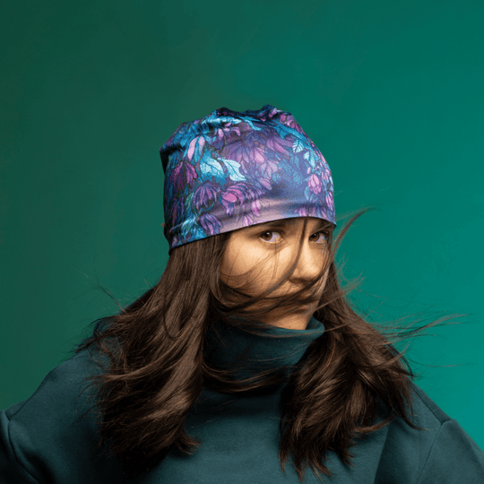 A young woman with long dark hair wearing the Wisteria beanie and a dark teal turtleneck, with her hair blowing around her face.