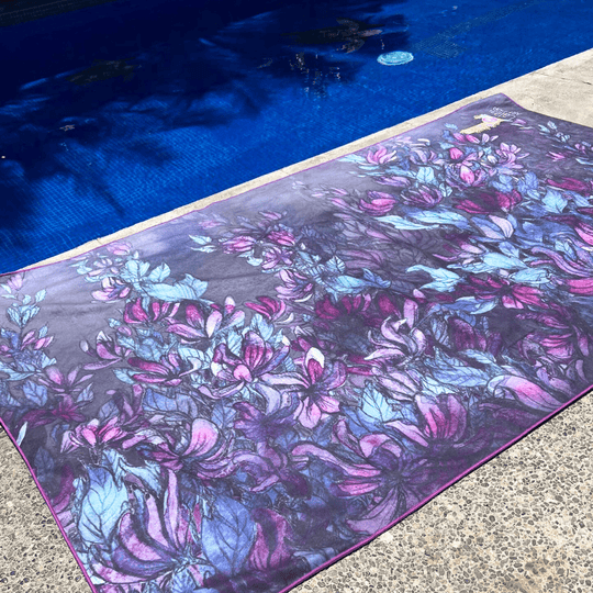 Wisteria Luxury Microfiber Towel spread out by a blue swimming pool, highlighting its vibrant floral art.