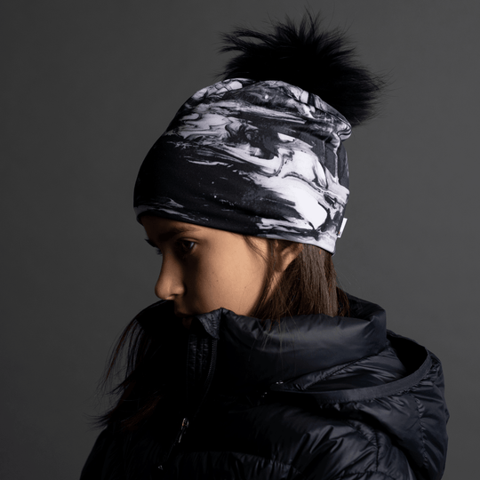 Close-up side profile of a young girl wearing the black and white abstract pattern beanie, looking down.