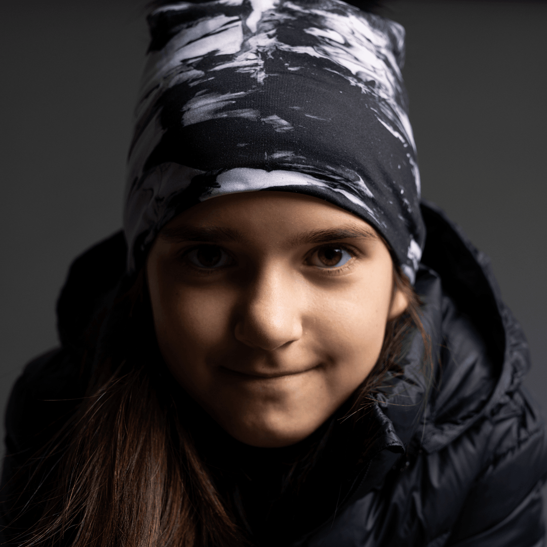 Young girl wearing the black and white abstract pattern beanie, looking forward.