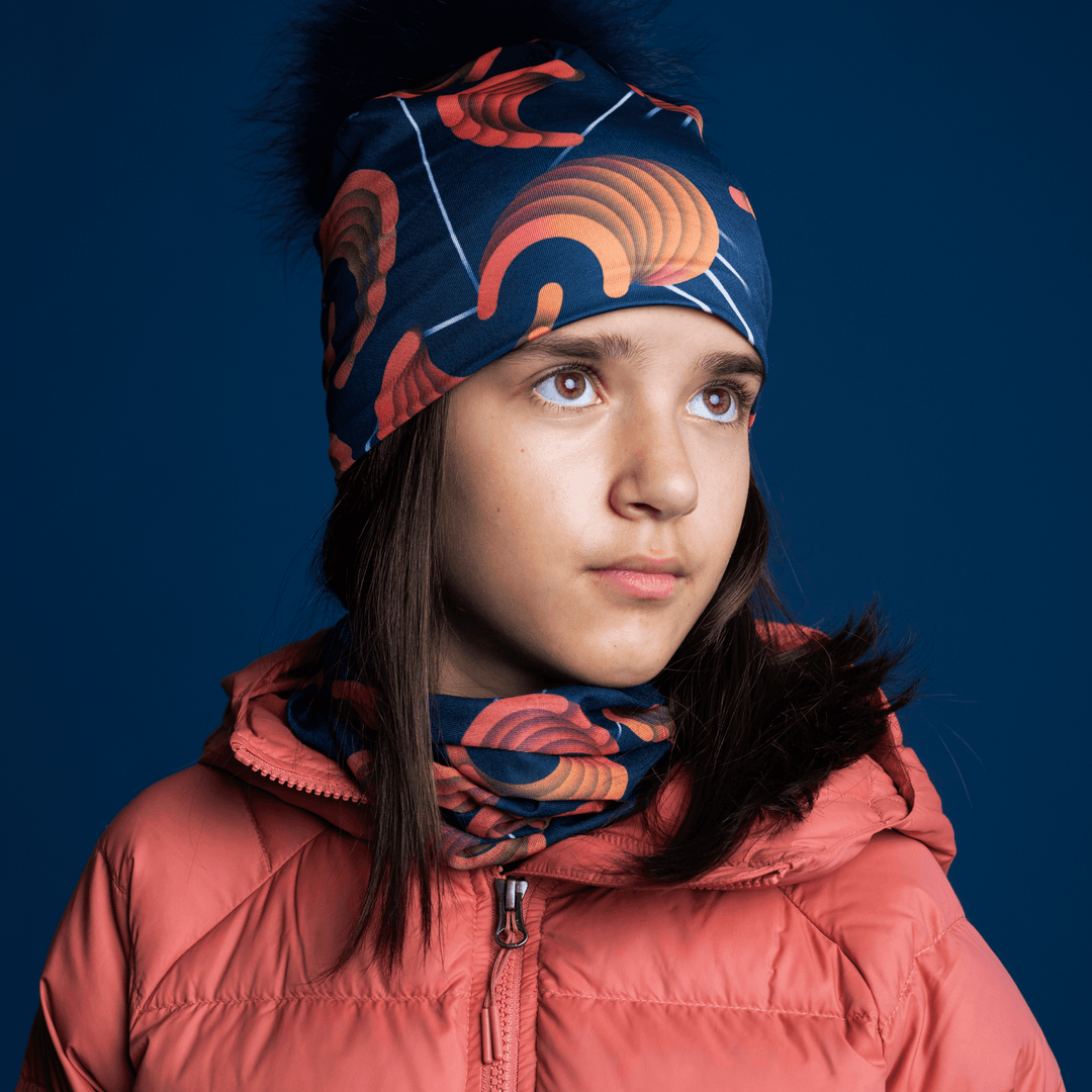 Young girl looking up and to the side, wearing the navy beanie with orange pattern and a matching neck gaiter