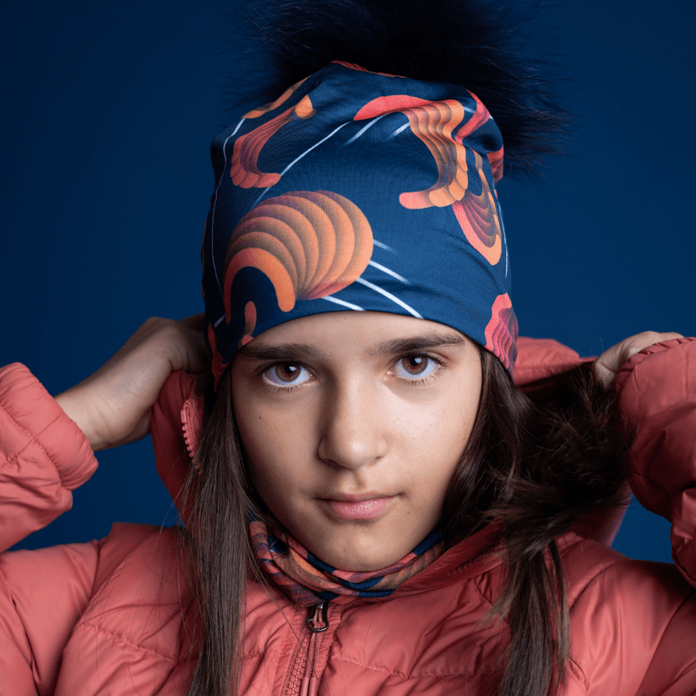 Young girl wearing a pink puffer jacket, the navy beanie with orange pattern, and a matching neck gaiter