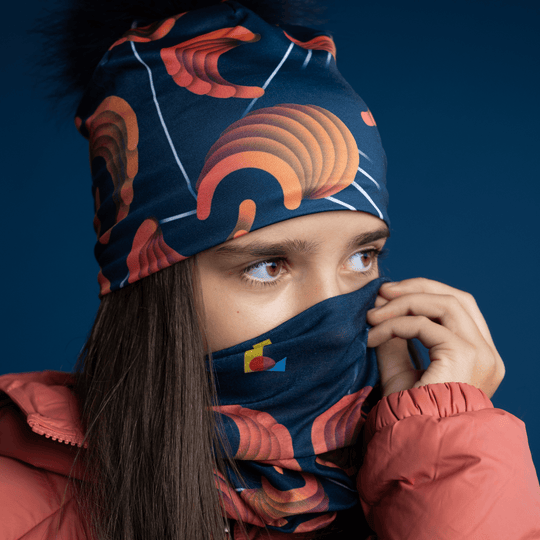 Young girl pulling the navy beanie with orange pattern up over her nose, with a matching neck gaiter visible
