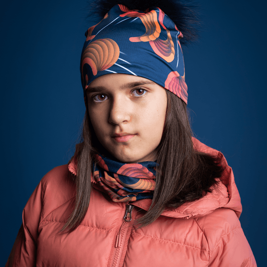 Young girl looking forward, wearing the navy beanie with orange pattern and a matching neck gaiter