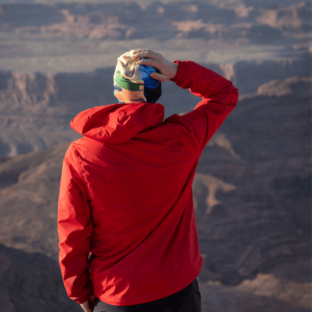Man in a red jacket wearing the abstract art beanie, looking out at a mountainous landscape.