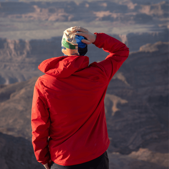 Man in a red jacket wearing the abstract art beanie, looking out at a mountainous landscape.
