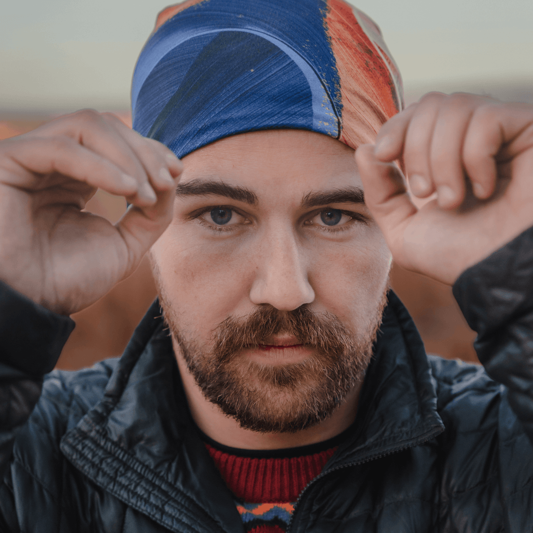 Close-up portrait of a man wearing the abstract art beanie, with hands near his face.