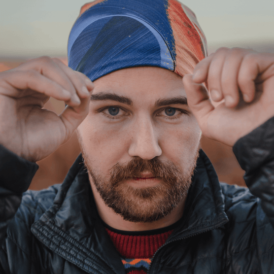 Close-up portrait of a man wearing the abstract art beanie, with hands near his face.