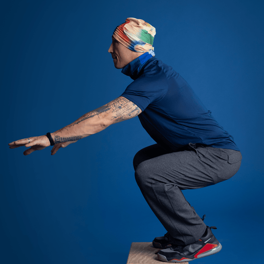 Man wearing the abstract art beanie and neck tube, performing a squat exercise.