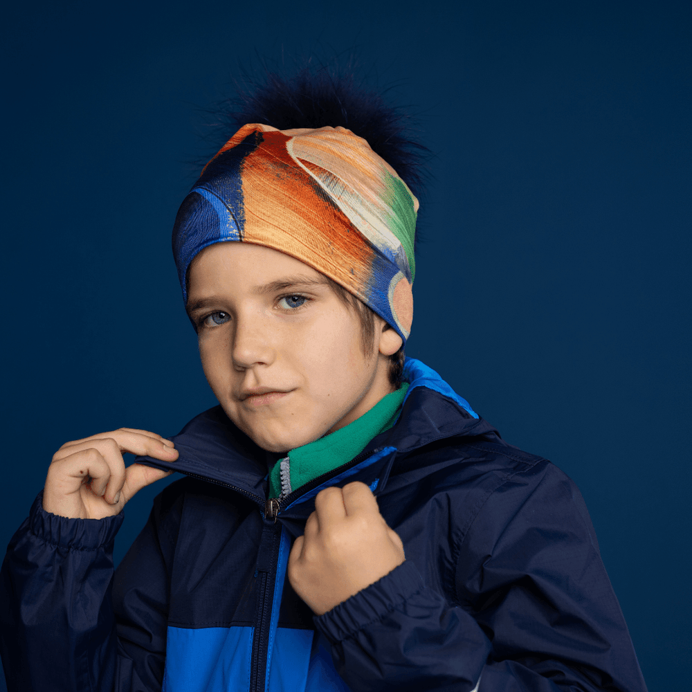Young boy wearing the Yellow & Blue Beanie with removable navy fur pom, styled with a jacket.