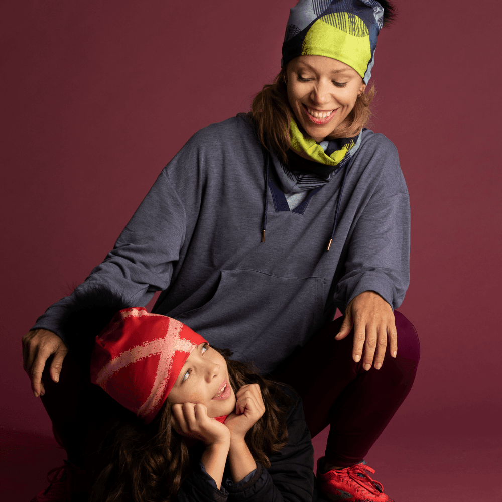 Mother and child wearing matching Yellow-Dots beanies and neck tubes in a studio setting.