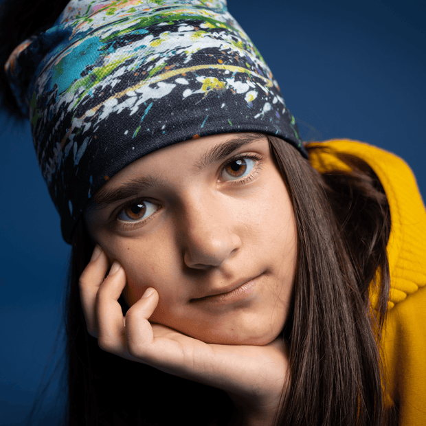 Young girl from the front wearing the Meduse hat designed by Megane Fortin. This beanie is black with green, blue, white and orange abstract patterns