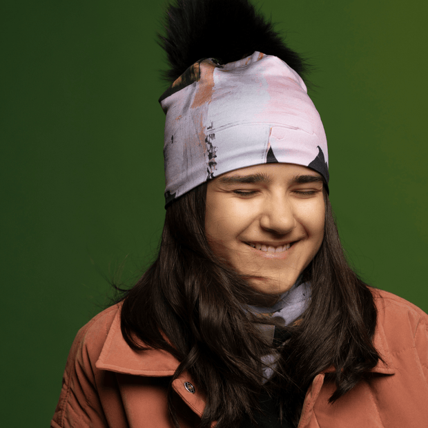 Laughing teenager wearing the Blush and Black Modern Quilt Beanie with Black Pompom by Catherine Parent for the Lalita's Art Shop 25 collection